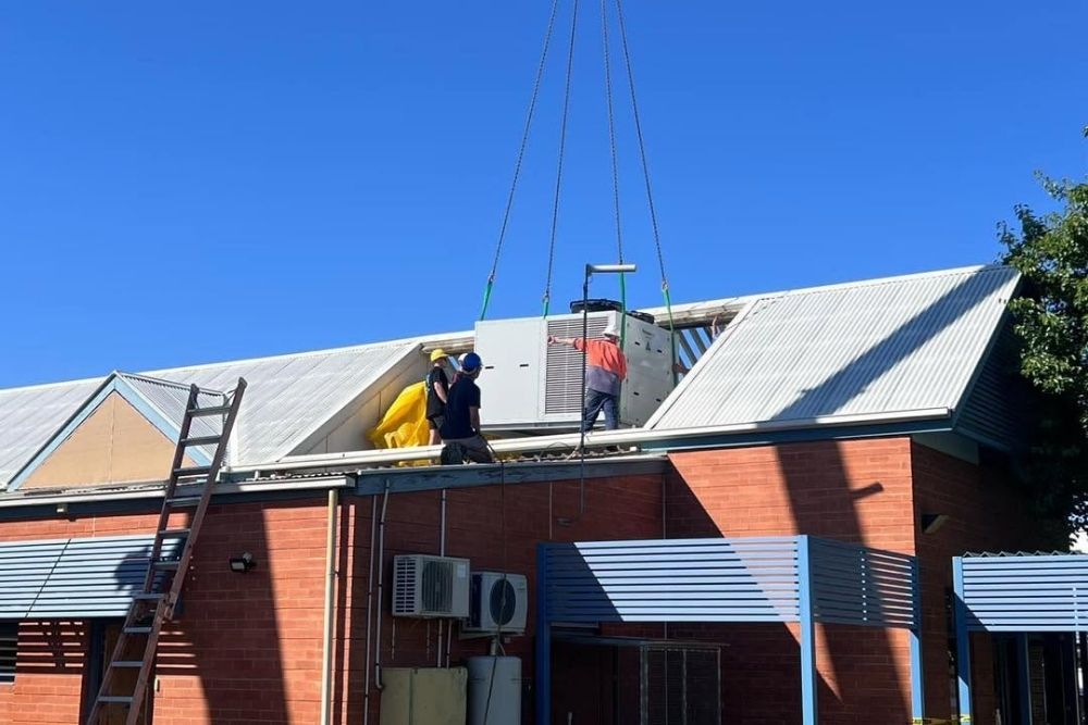 Crane lowering a commercial HVAC unit onto a building roof